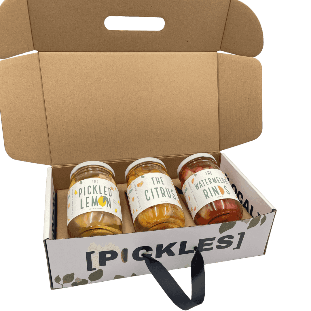 Unboxed set of three glass jars with colorful labels of pickled lemon, citrus, and watermelon rinds, inside a cardboard container