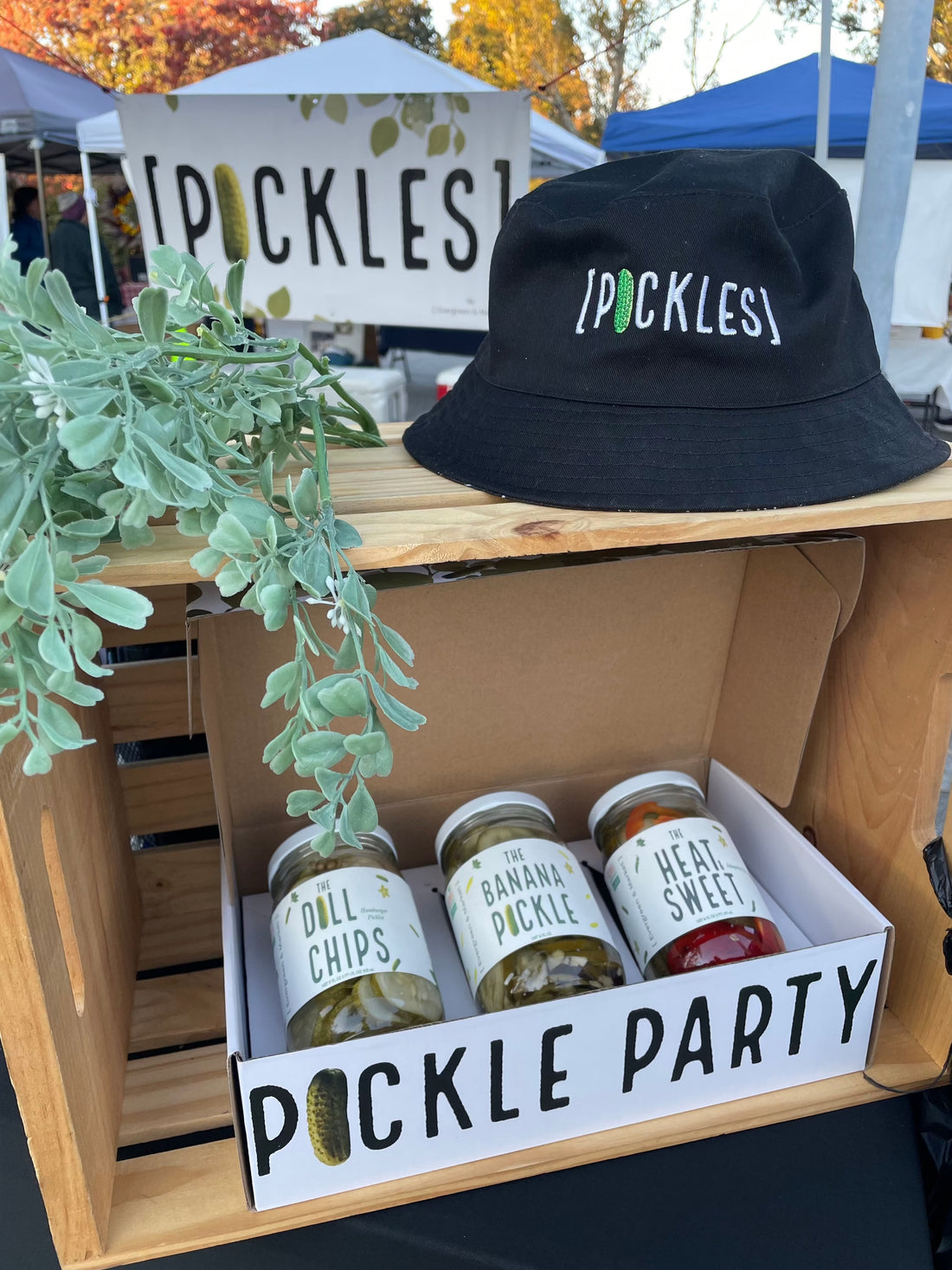Market stall with jars of pickled products, a sign reading 'Pickle Party,' and a black bucket hat with the 'Pickles' logo in front.