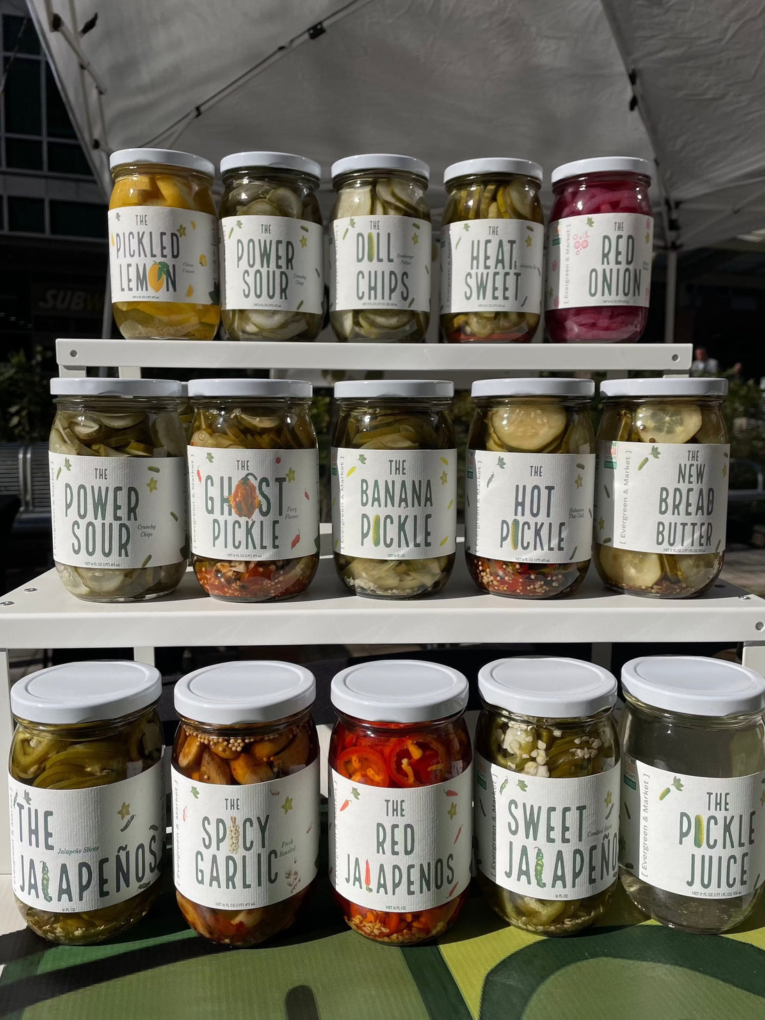 Shelves of pickle jars at a market stall, including Power Sour, Ghost Pickle, Banana Pickle, Hot Pickle and Sweet Jalapeño