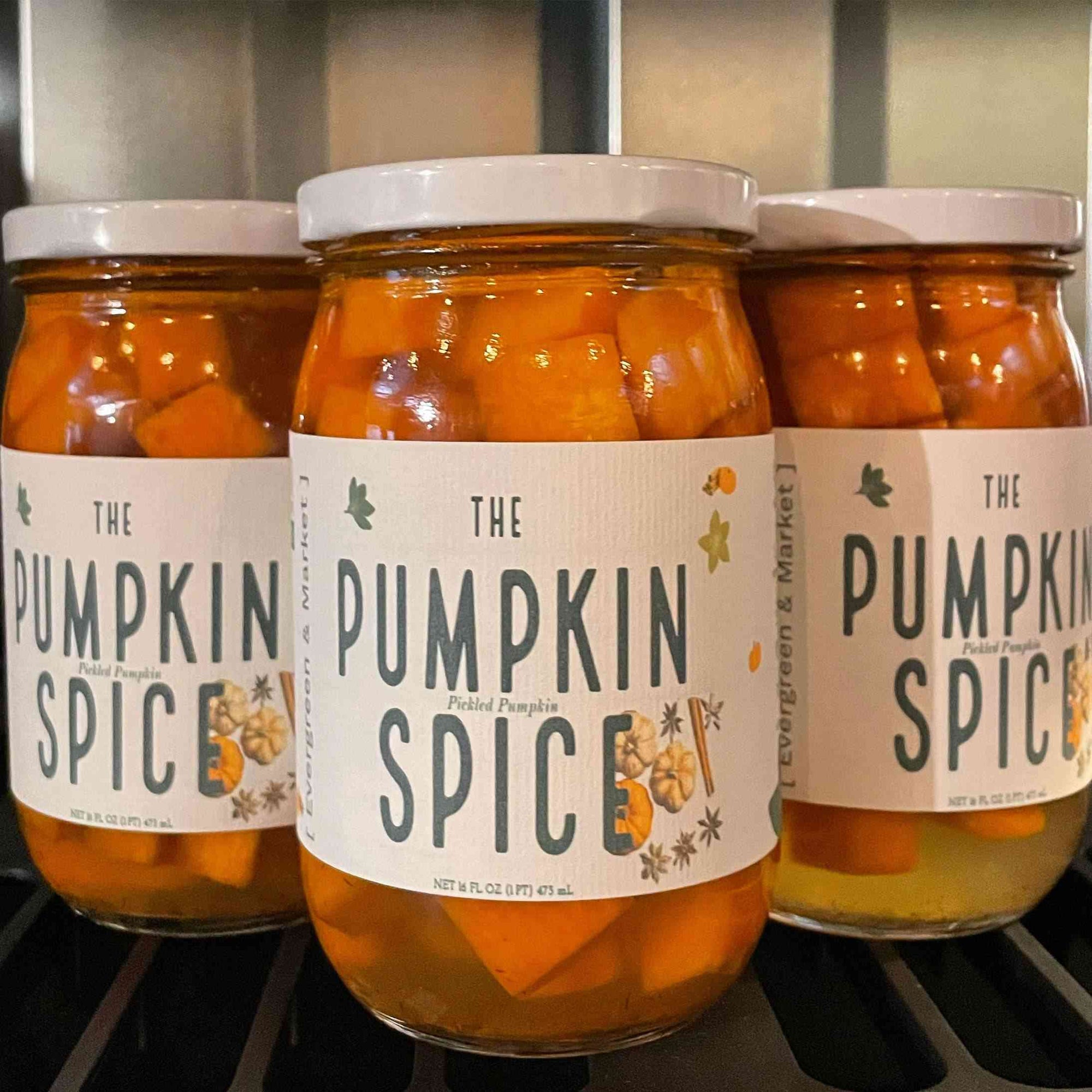Glass jar of pickled orange chunks with white lid, labeled 'Discover Delicious Pickled Things,' on a dark shelf, close-up shot