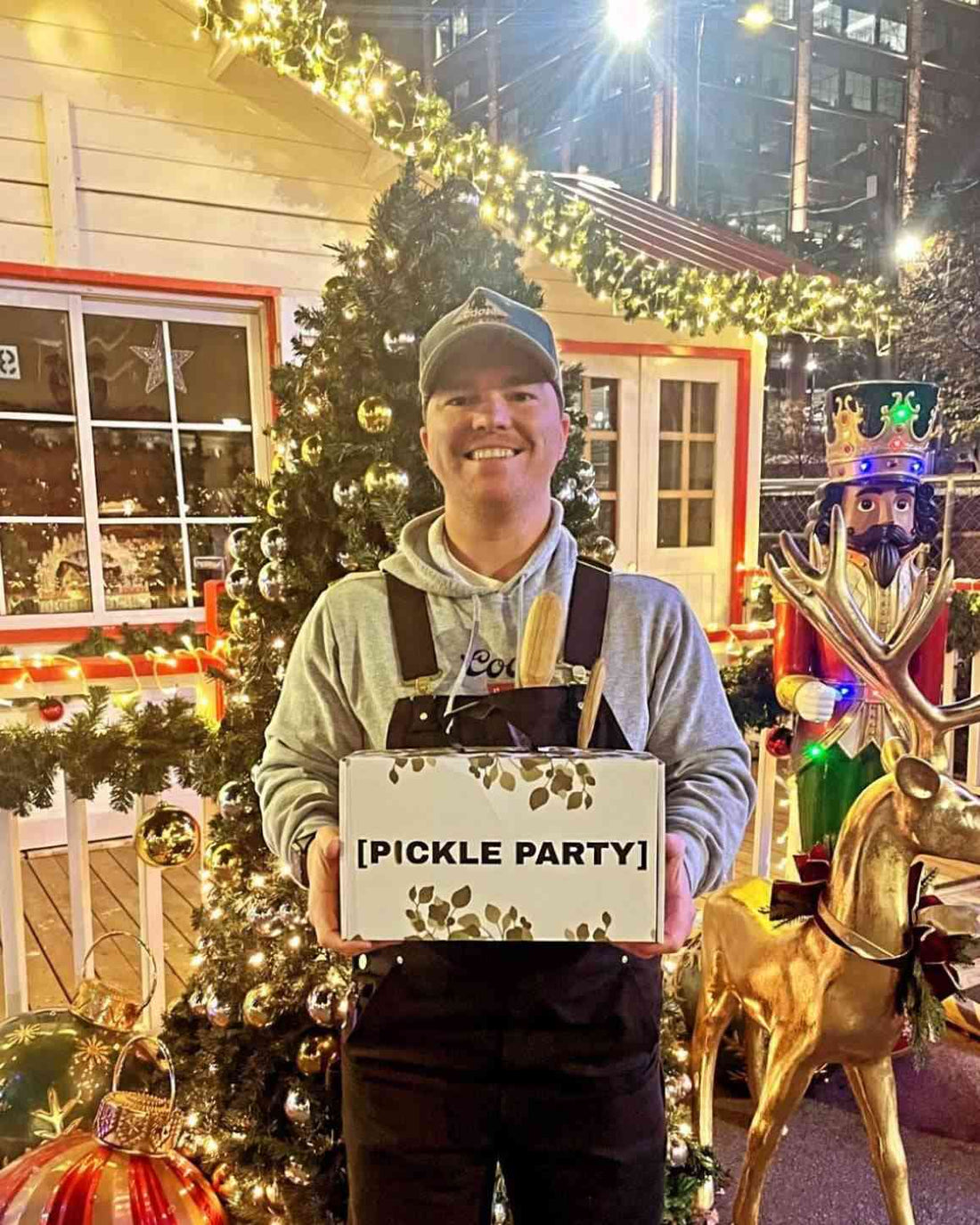 Man holding a Pickle Party gift box in front of a lit Christmas tree