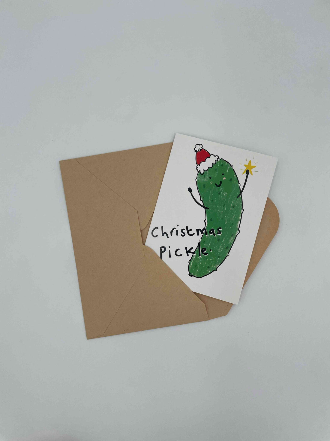 Christmas Pickle card with a pickle in a Santa hat holding a sparkler, on a kraft envelope
