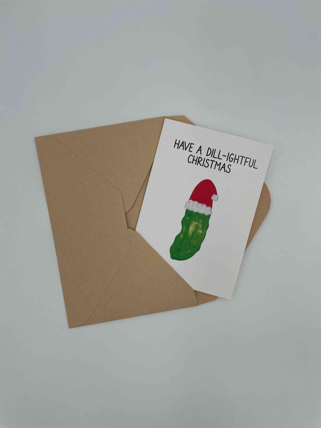 Have a Dill-ightful Christmas card with a pickle in a Santa hat, on a kraft envelope