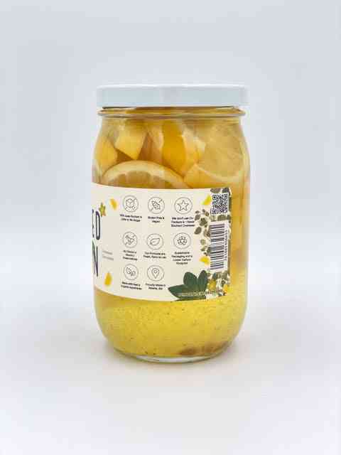 Back view of jar showing product label with icons and barcode, containing sliced lemons in pickling liquid for culinary use.