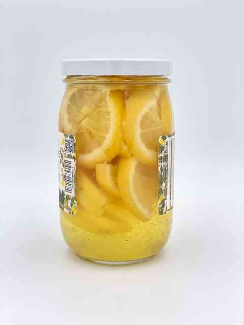 Side view of jar filled with lemon slices submerged in bright yellow pickling liquid, ideal for flavoring cocktails and salads.