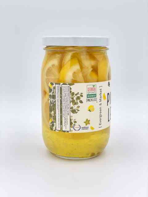 Rear view of jar displaying product label with branding, ingredients, and barcode, containing preserved lemon slices in pickled brine.