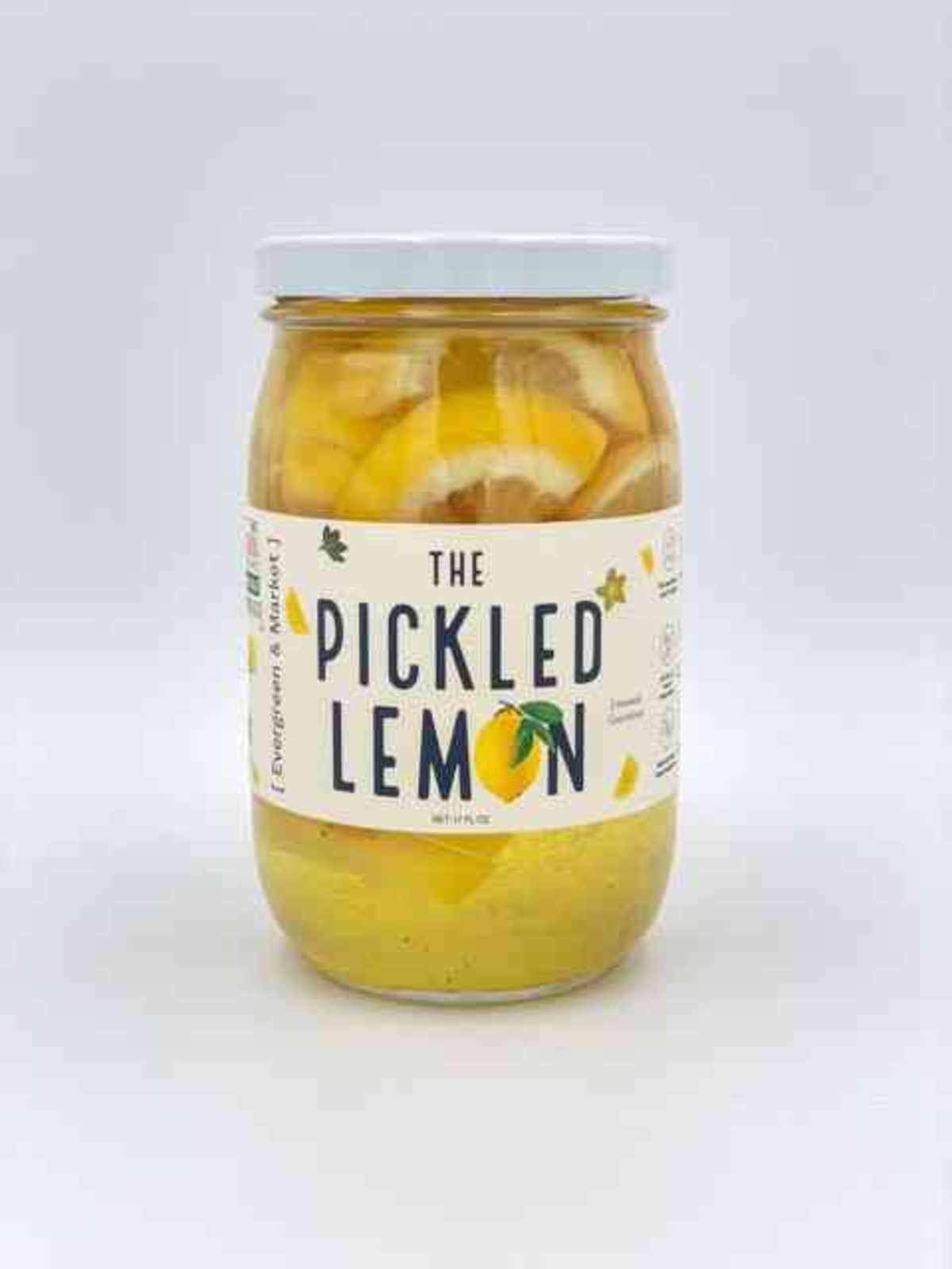 Glass jar of pickled lemons with lemon slices and peels in a tangy yellow brine, labeled 'The Pickled Lemon' for cocktails and salads.